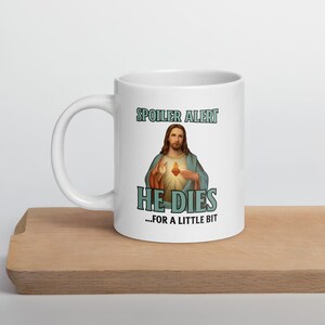 May include: White ceramic coffee mug with a blue and black graphic of Jesus with the text "Spoiler Alert He Dies...for a little bit"