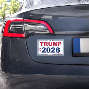 Puede incluir: Una pegatina rectangular con el texto "TRUMP $2028 per gallon" en rojo y azul sobre fondo blanco. La pegatina está adherida a la parte trasera de un coche gris oscuro, cerca del piloto trasero.