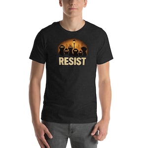 Puede incluir: Camiseta gris oscuro con la palabra "RESIST" en negrita. El diseño presenta siluetas de personajes de dibujos animados sobre un fondo de puesta de sol con una farola.