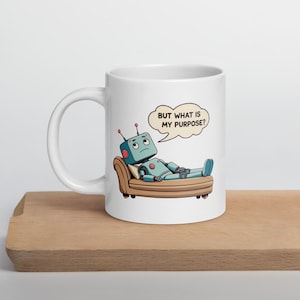 May include: White ceramic mug featuring a cartoon robot lounging on a brown couch. The robot is blue with red antennae and a speech bubble that reads, "BUT WHAT IS MY PURPOSE?" The mug is on a wooden surface.