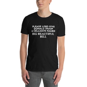 May include: Black t-shirt with white text that reads: "PLEASE LORD GIVE DONALD TRUMP A CELLMATE NAMED BIG BEAUTIFUL BILL". The shirt is worn by a person in a medium shot.