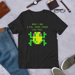 May include: A dark heather grey t-shirt with a pixelated green frog graphic and the text "WHEN I WAS A KID, FROGS LOOKED LIKE THIS."