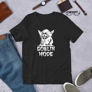 May include: A dark heather grey t-shirt with a white graphic of a goblin with the text "Goblin Mode" underneath.