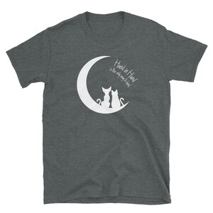 May include: A dark heather grey t-shirt with a white crescent moon and two cats sitting back to back on the moon. The text "Hand in Hand is the only way to lead" is printed on the shirt.