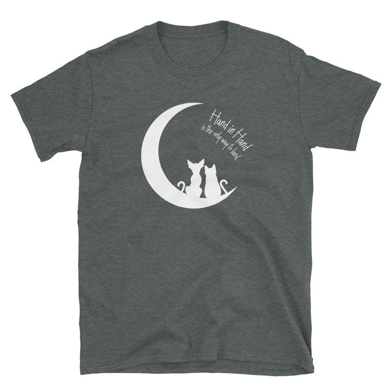May include: A dark heather grey t-shirt with a white crescent moon and two cats sitting back to back on the moon. The text "Hand in Hand is the only way to lead" is printed on the shirt.