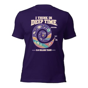 Könnte beinhalten: Ein dunkelviolettes Kurzarm-T-Shirt mit einer Grafik einer spiralförmigen Zeitleiste des Universums. Der Text lautet I THINK IN DEEP TIME, BIG BANG, EARTH FORMS, PRESENT, HUMAN HISTORY und 13.8 BILLION YEARS mit farbenfrohen Illustrationen.