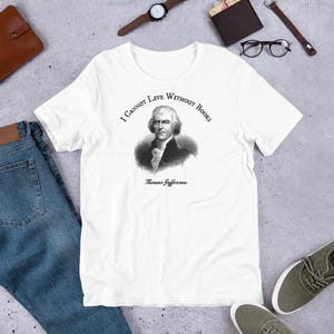 May include: White t-shirt with a black and white image of Thomas Jefferson and the quote "I cannot live without books".