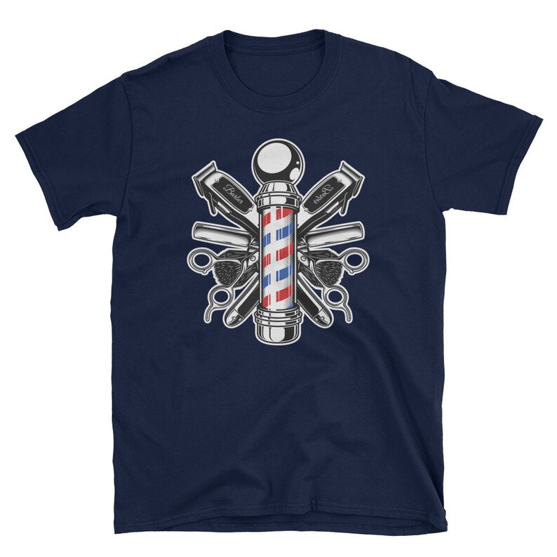Puede incluir: Camiseta azul marino con una ilustraci&oacute;n vintage de un poste de barbero rodeado de herramientas de barbero cruzadas. El poste de barbero es rojo, blanco y azul con una base plateada. Las herramientas incluyen cortadoras, navajas y un peine.