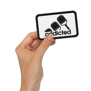 May include: Black and white patch with a pickleball paddle design and the text "addicted".