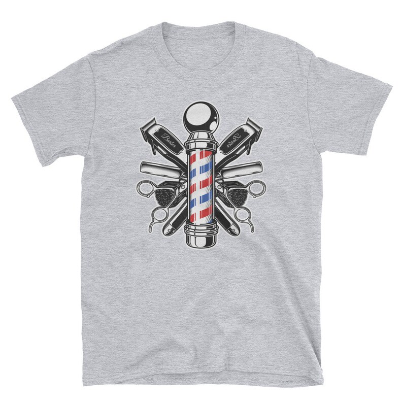 Puede incluir: Una camiseta gris con una ilustraci&oacute;n vintage de un poste de barbero rodeado de herramientas de barbero, incluyendo tijeras, navajas y peines. El poste de barbero es rojo, blanco y azul.