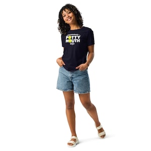 Peut inclure: Un t-shirt bleu marine avec le texte "pickleball POTTY MOUTH" en blanc et jaune. Le modèle porte un short en jean et des sandales blanches. Le t-shirt présente un graphisme de pickleball.