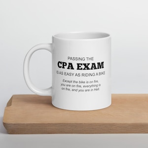 Könnte beinhalten: Ein weißer Keramikbecher mit Henkel, der mit schwarzem Text bedruckt ist: PASSING THE CPA EXAM IS AS EASY AS RIDING A BIKE. Except the bike is on fire, you are on fire, everything is on fire, and you are in Hell.