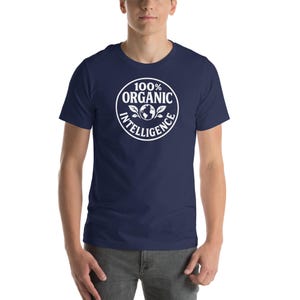 May include: Navy blue t-shirt with a white circular graphic that reads "100% ORGANIC INTELLIGENCE". The graphic features a globe and leaves. The shirt is a short-sleeved crew neck.