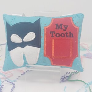 May include: A turquoise pillow with a white tooth wearing a black mask and a red sign that says "My Tooth".