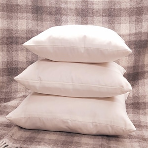 May include: Three white cotton pillow covers stacked on top of each other. The pillow covers are all the same size and shape.