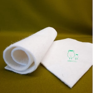 May include: A roll of white wool felt with a smaller piece of felt with the logo "UANWOOL" and two sheep with bows on their heads.