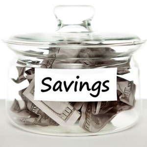 May include: A glass jar with a lid filled with crumpled dollar bills. A white label on the front of the jar reads "Savings".