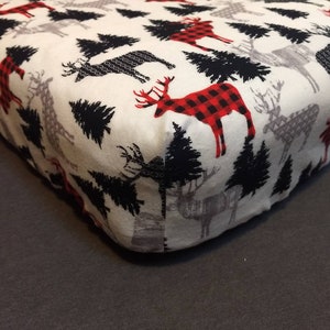 May include: White fitted sheet with a repeating pattern of black trees and red and black checked deer.