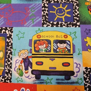 May include: A colourful fabric featuring a school bus theme. The bus is yellow with black windows and the words "SCHOOL BUS" on the side. There are stars, a handprint, and a sun with a smiley face on the fabric.