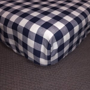 Op de afbeelding: Een hoeslaken met een wit en donkerblauw ruitjespatroon. Het laken is gemaakt van een zachte, comfortabele stof en is perfect om elke slaapkamer een vleugje stijl te geven.