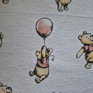 Puede incluir: Tela blanca con un patrón repetido de un oso de dibujos animados en varias poses, incluyendo uno sosteniendo un globo rosa. El oso lleva una camisa rosa y el globo también es rosa.