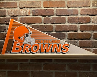 Puede incluir: Un banderín marrón y naranja con el logotipo de los Cleveland Browns. El logotipo presenta un casco de fútbol y el nombre del equipo en letras blancas y negritas.