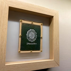 May include: A framed green leather patch with gold tacks and a white seal that reads "Manhattan College, New York" and "Manhattan".