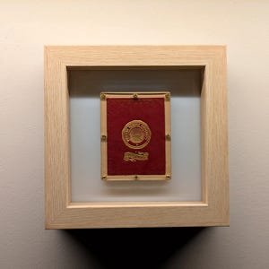 May include: A framed red and gold card with a gold emblem and the text "The Royal Game of Cards" in a light wood frame.