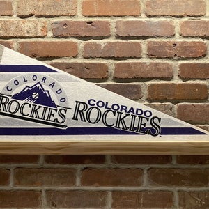 May include: A white pennant with blue stripes and the words "Colorado Rockies" in black and blue lettering. The pennant features a logo of the Rocky Mountains with a baseball inside.