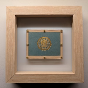 May include: A framed print of a blue and gold seal with the text "University of Maine" inside a wooden frame.