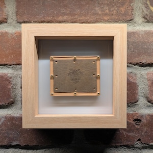 Könnte beinhalten: Ein gerahmtes Kunstwerk mit braunem Lederhintergrund und goldenem Design. Der Rahmen ist aus hellem Holz.