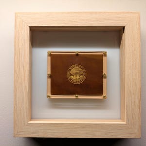 Peut inclure: Une œuvre d'art encadrée avec un sceau doré au centre. Le sceau représente un bâtiment avec un dôme et le texte "The United States Capitol Washington D.C."