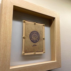 May include: A framed document with a blue seal and the text "Universitatis Albrechtianae Sigillum" and "Alfred". The frame is made of light wood.