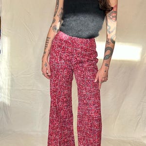 May include: A woman wearing a black fuzzy tank top and red and white patterned flared trousers. She is standing in front of a white background.