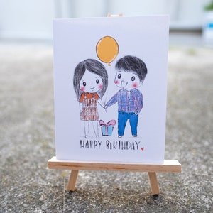 Puede incluir: Una tarjeta blanca con una ilustraci&oacute;n dibujada a mano de una pareja que se toma de la mano con un globo amarillo y una caja de regalo. El texto "Happy Birthday" est&aacute; escrito debajo de la ilustraci&oacute;n.