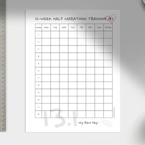 Könnte beinhalten: Ein weißes 12-Wochen-Halbmarathon-Trainingsdiagramm mit einem Raster zur Verfolgung von Läufen. Der Text "12-WEEK HALF MARATHON TRAINING 13.1" steht oben. Ein Metalllineal, ein Stift und eine Kaffeetasse sind ebenfalls im Bild.