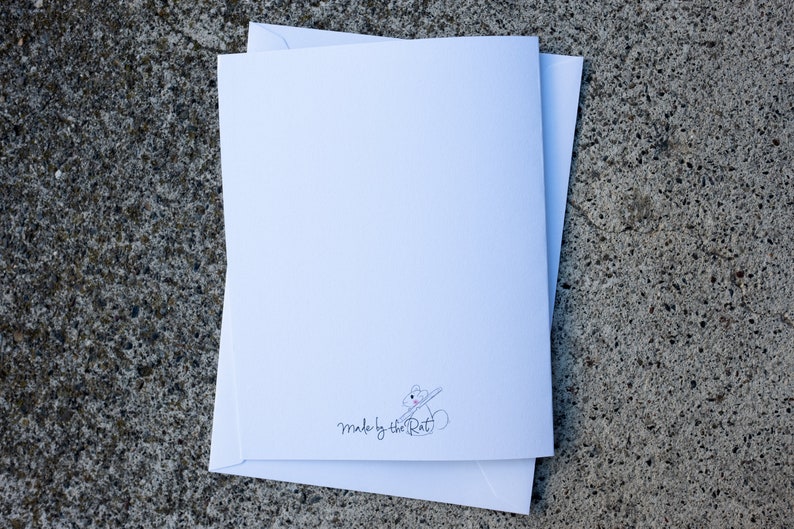 Puede incluir: Tarjeta blanca en blanco con una peque&ntilde;a ilustraci&oacute;n de un conejo sosteniendo un pincel y el texto "made by the Rat" en cursiva negra.