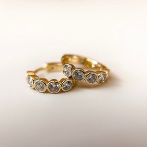 May include: A pair of gold hoop earrings with clear round stones set along the edge of each hoop.