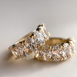 May include: Two gold rings with oval-shaped clear gemstones. The rings are stacked on top of each other.
