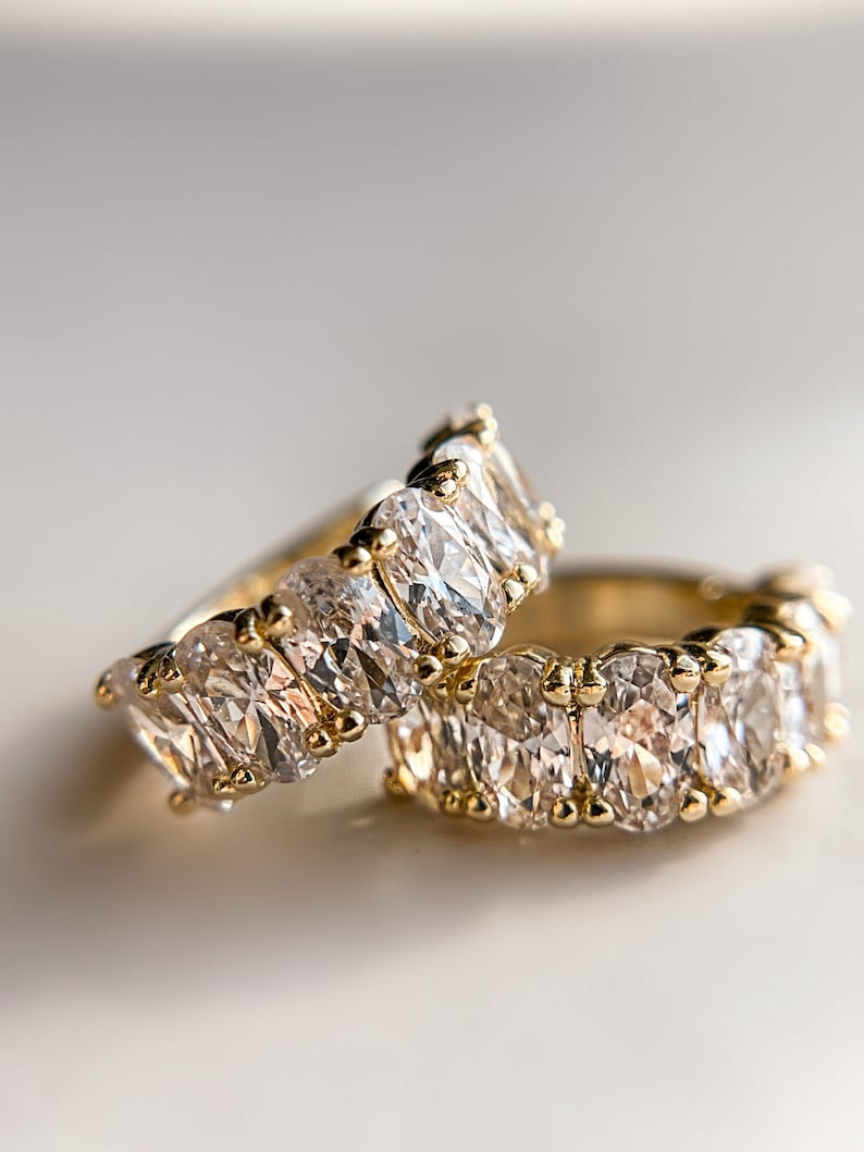 May include: Two gold rings with oval-shaped clear gemstones. The rings are stacked on top of each other.
