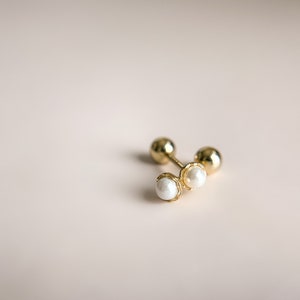 Op de afbeelding: Een paar gouden oorbelletjes met kleine witte parel accenten.