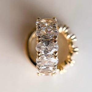 May include: A gold ring with a row of five oval-shaped clear stones.