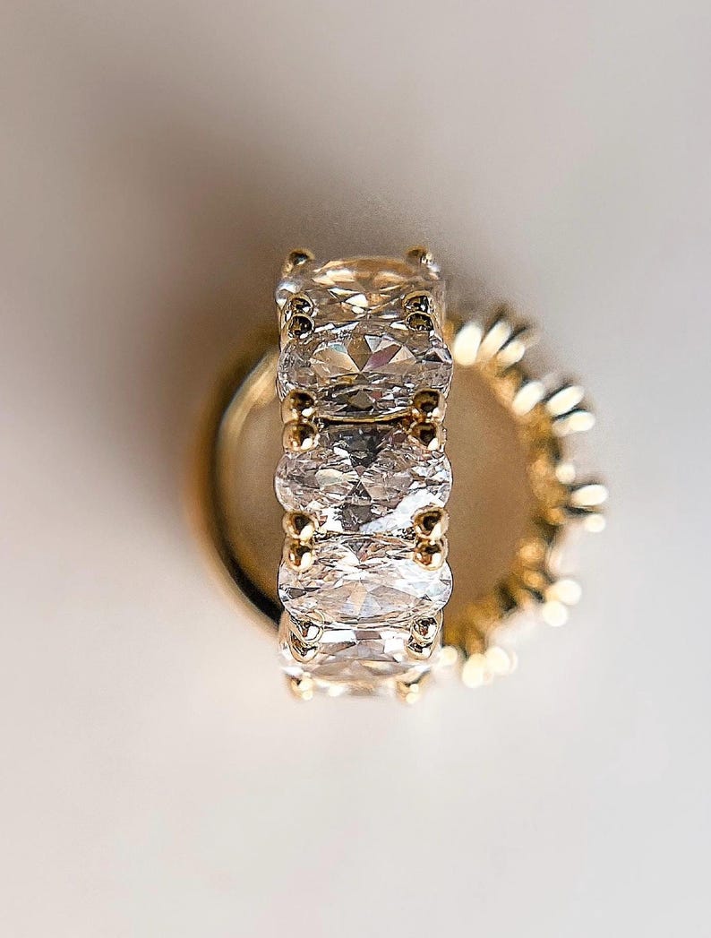 May include: A gold ring with a row of five oval-shaped clear stones.