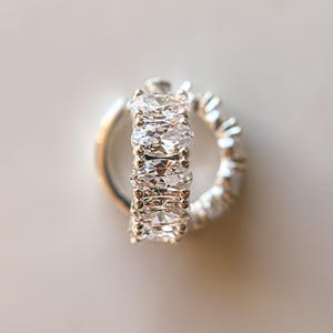 May include: A silver hoop earring with a row of clear oval-shaped cubic zirconia stones.