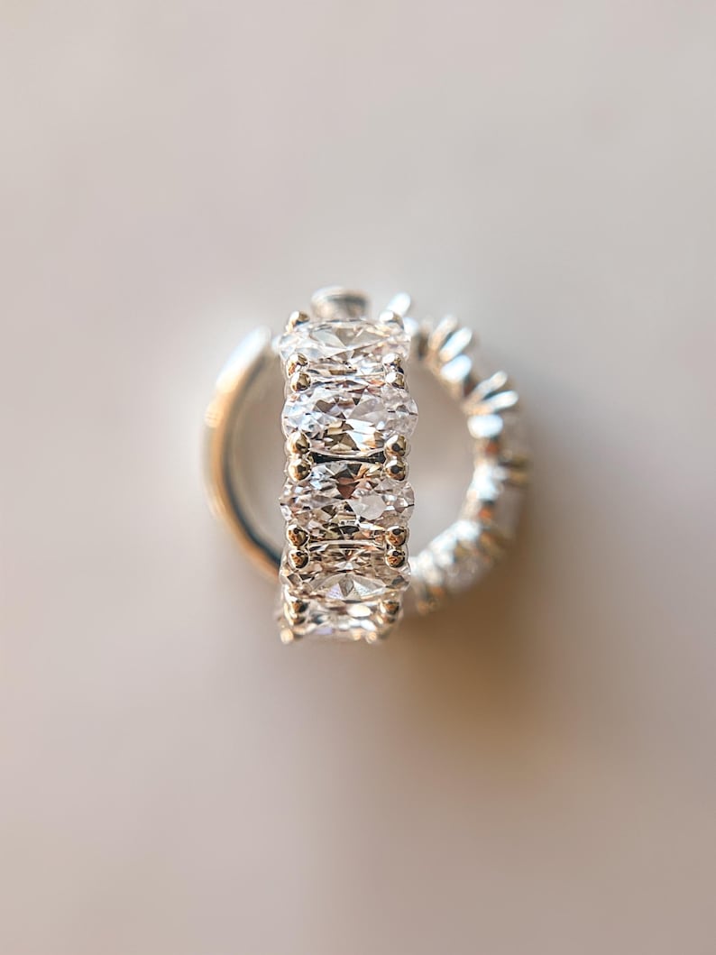 May include: A silver hoop earring with a row of clear oval-shaped cubic zirconia stones.