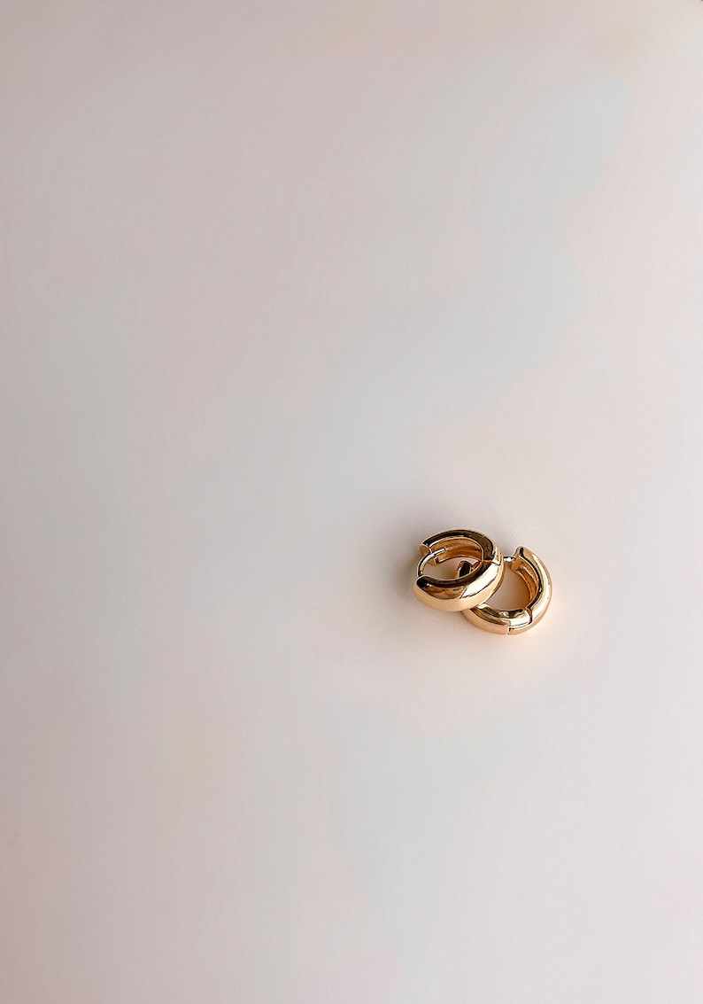 May include: A pair of gold hoop earrings. The hoops are thick and have a smooth, polished finish.