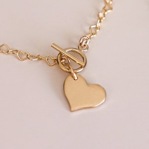 以下が含まれることがあります： 小さなハートが連なったチェーンに、ハート型のチャームがついたゴールドのネックレス。留め具はトグル式です。