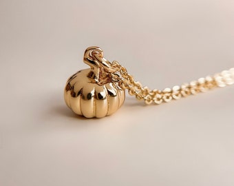 May include: A gold-colored necklace with a small, detailed pumpkin pendant. The chain is delicate and the pumpkin is a simple, classic design.