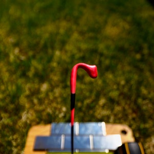 May include: A close-up of a red and black fishing bobber with a curved top. The bobber is held in a hand over a metal surface.