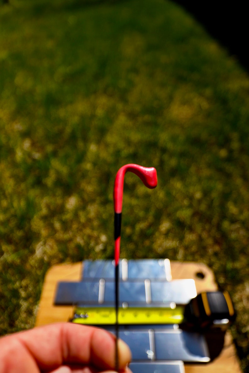 May include: A close-up of a red and black fishing bobber with a curved top. The bobber is held in a hand over a metal surface.